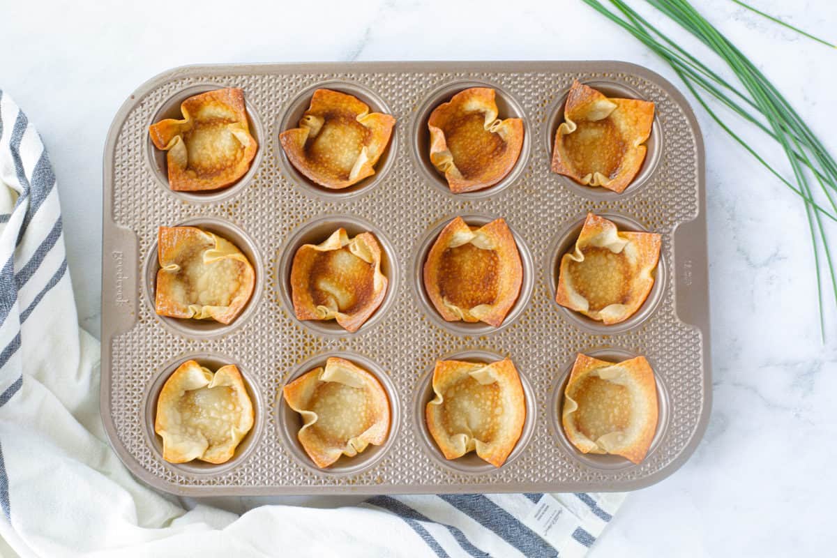 Baked wonton wrappers in a 12 cup muffin tin after being baked into "cups".