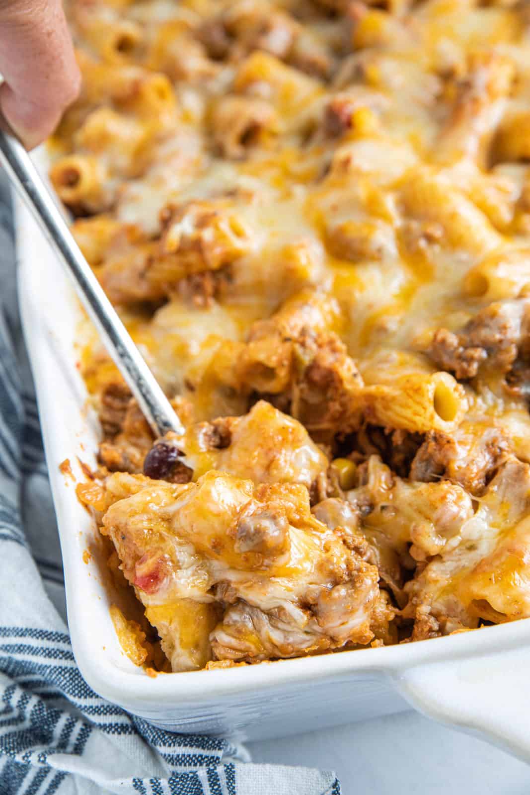 Cheesy Taco Pasta in a casserole dish with a serving being scooped out of the dish with a spoon. 