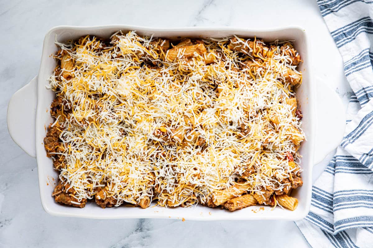 Cheesy Taco Pasta in a 9 x 13 casserole dish topped with shredded cheese on a granite countertop with a dish towel next to the baking pan.