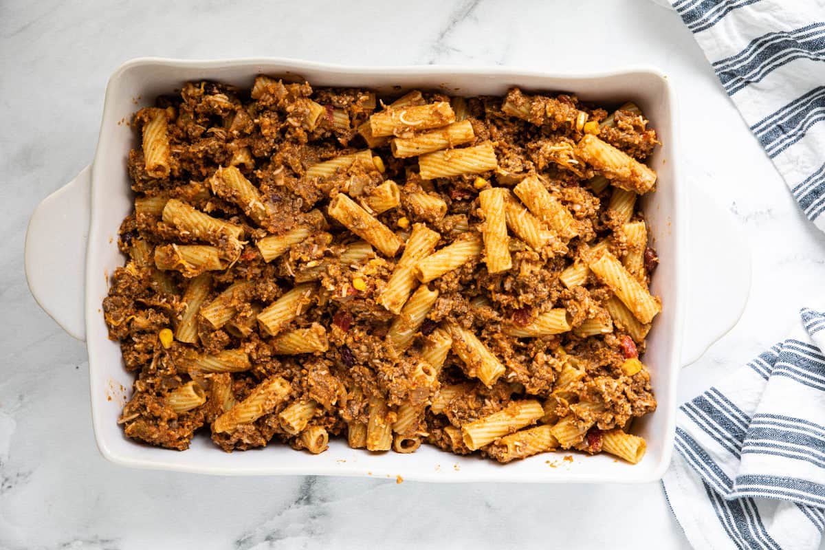 Cheesy Taco Pasta in a 9 x 13 casserole dish on a granite countertop with a dish towel next to the baking pan.