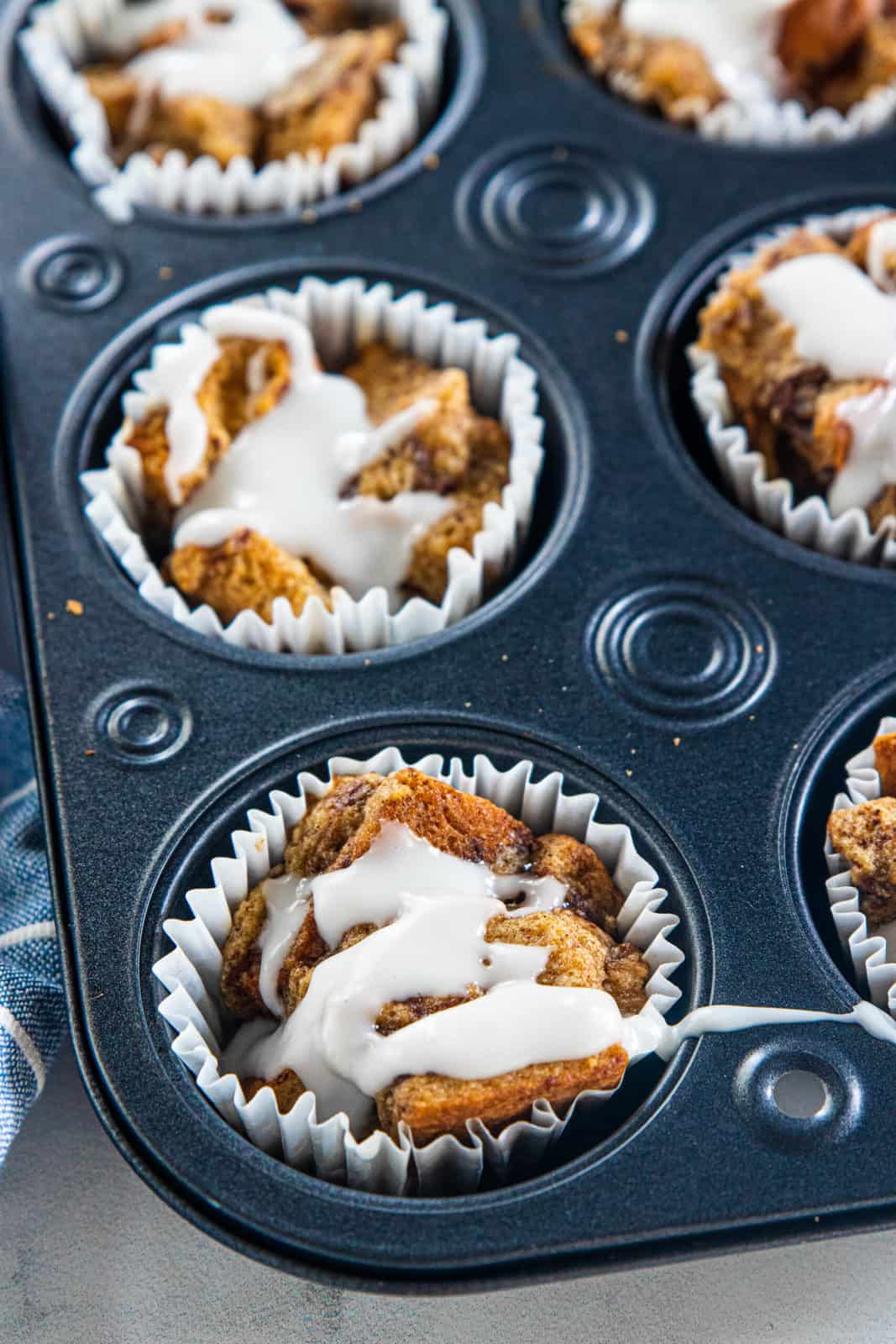 Baked French toast muffins in a muffin tin with glaze drizzled over the top.