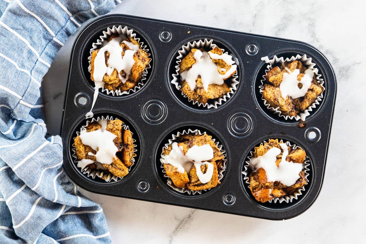 French toast muffins in a muffin tin with glazed drizzled over the top of the muffins. 