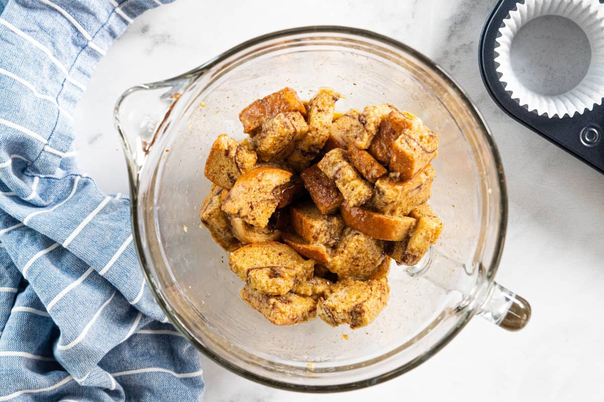 Bread cubes mixed with muffin batter in a glass mixing bowl.