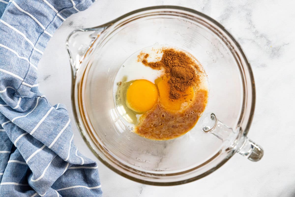 Muffin batter ingredients in a glass mixing bowl with a blue dish towel next to the bowl all on top of a granite countertop. 