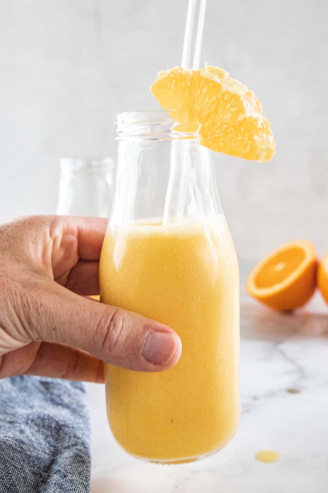 A hand holding a glass jar with a straw filled with orange smoothie. 