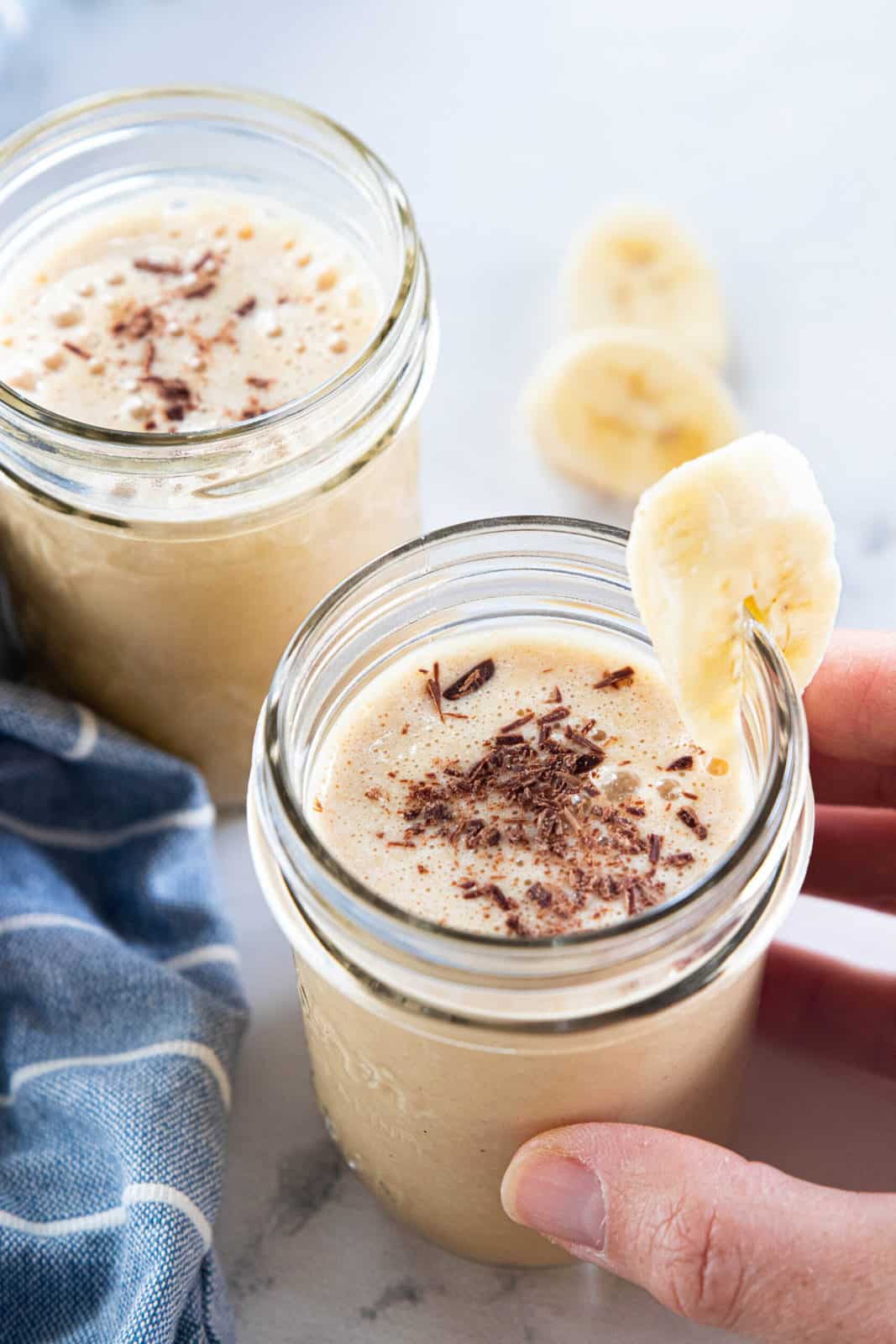 Two peanut butter powder smoothies in glasses with a slice of banana on the side of one glass. 