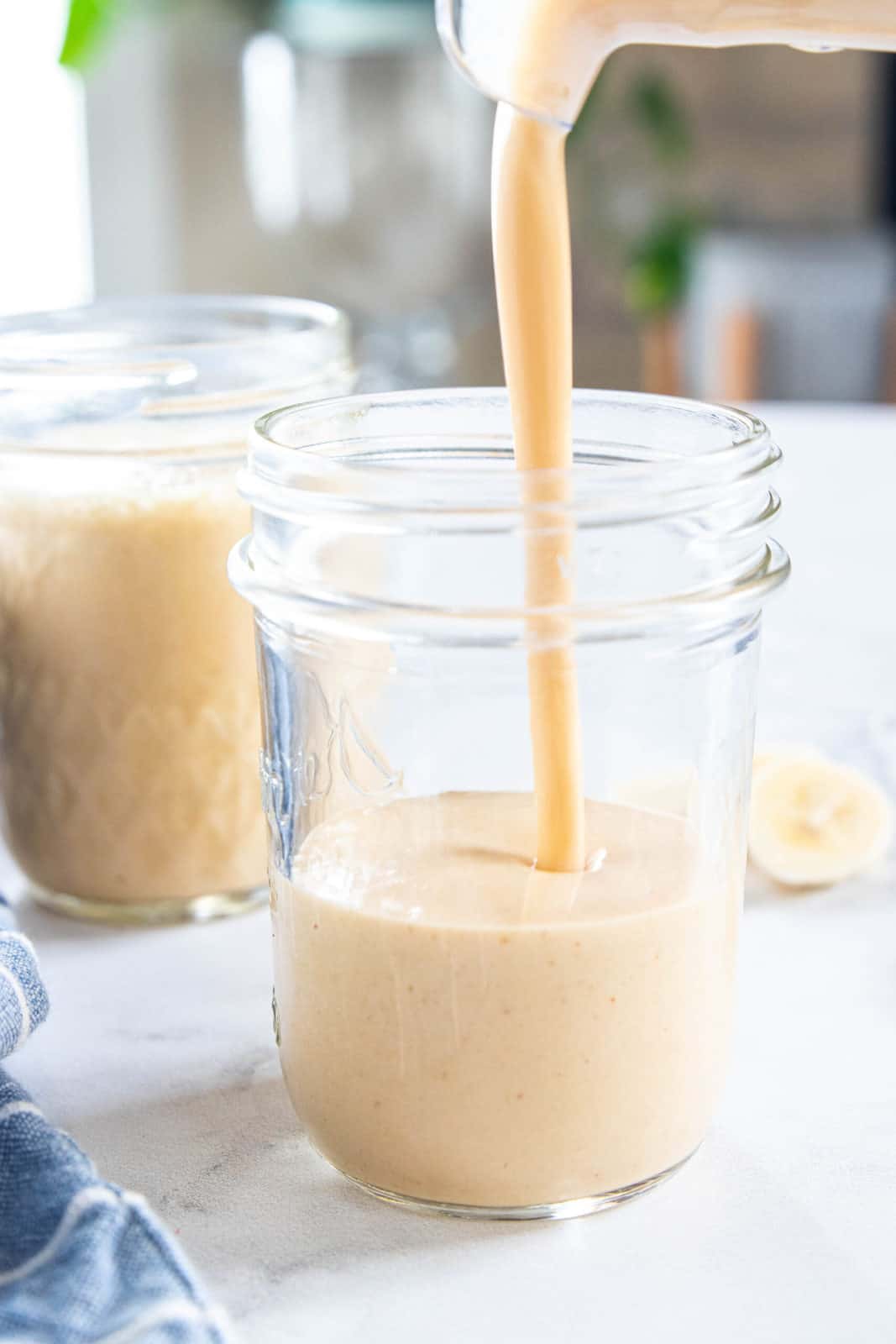 One full glass of a peanut butter smoothie with another glass being filled with smoothie from the blender.