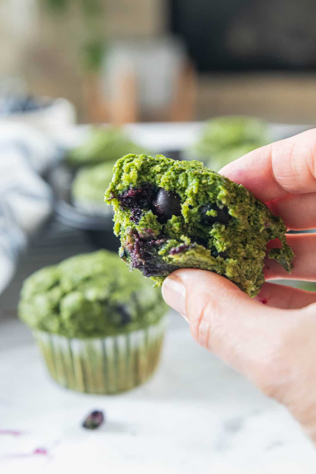 A half of a spinach muffin with bananas and blueberries being held in a hand.