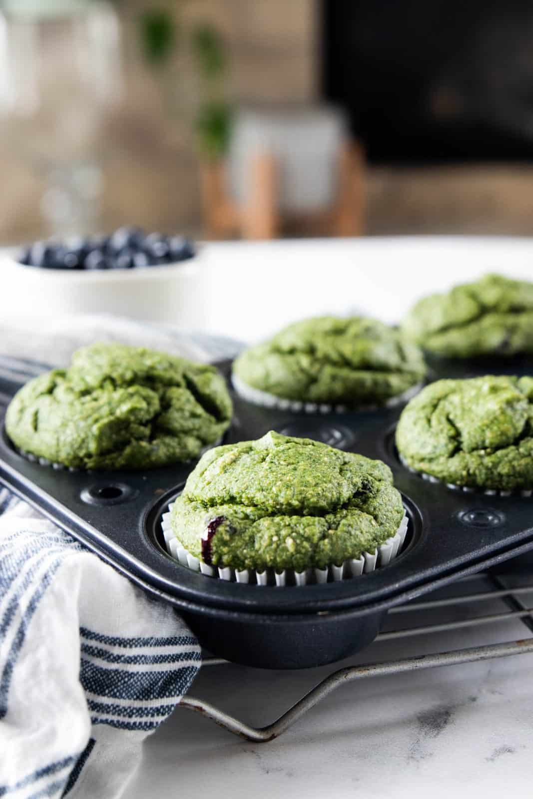 A muffin tin of cooked veggie muffins on a cooling rack next to a dish towel all on top of a granite countertop.