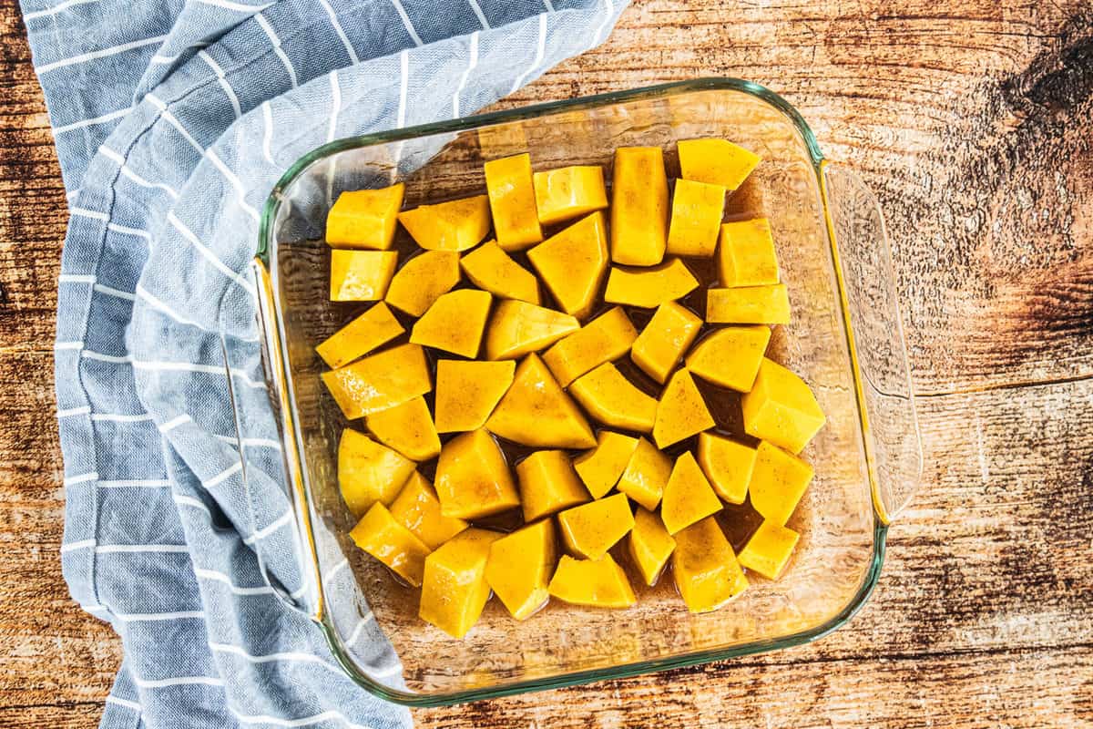 Chopped butternut squash in a glass dish with a maple sauce poured over the top. 
