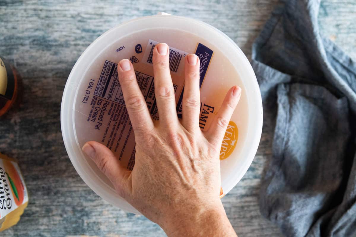 A hand placing a lid on to of an ice cream pail.