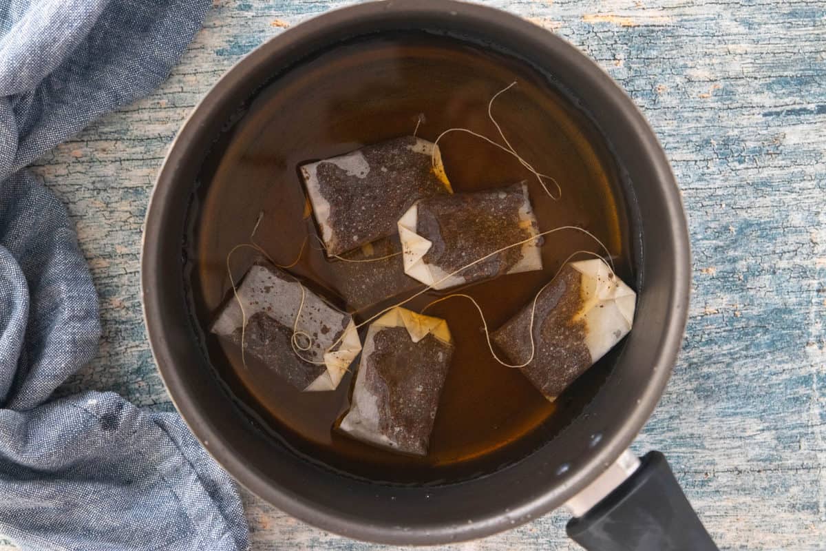 Six tea bags steeping in a large pot filled with boiling water. 