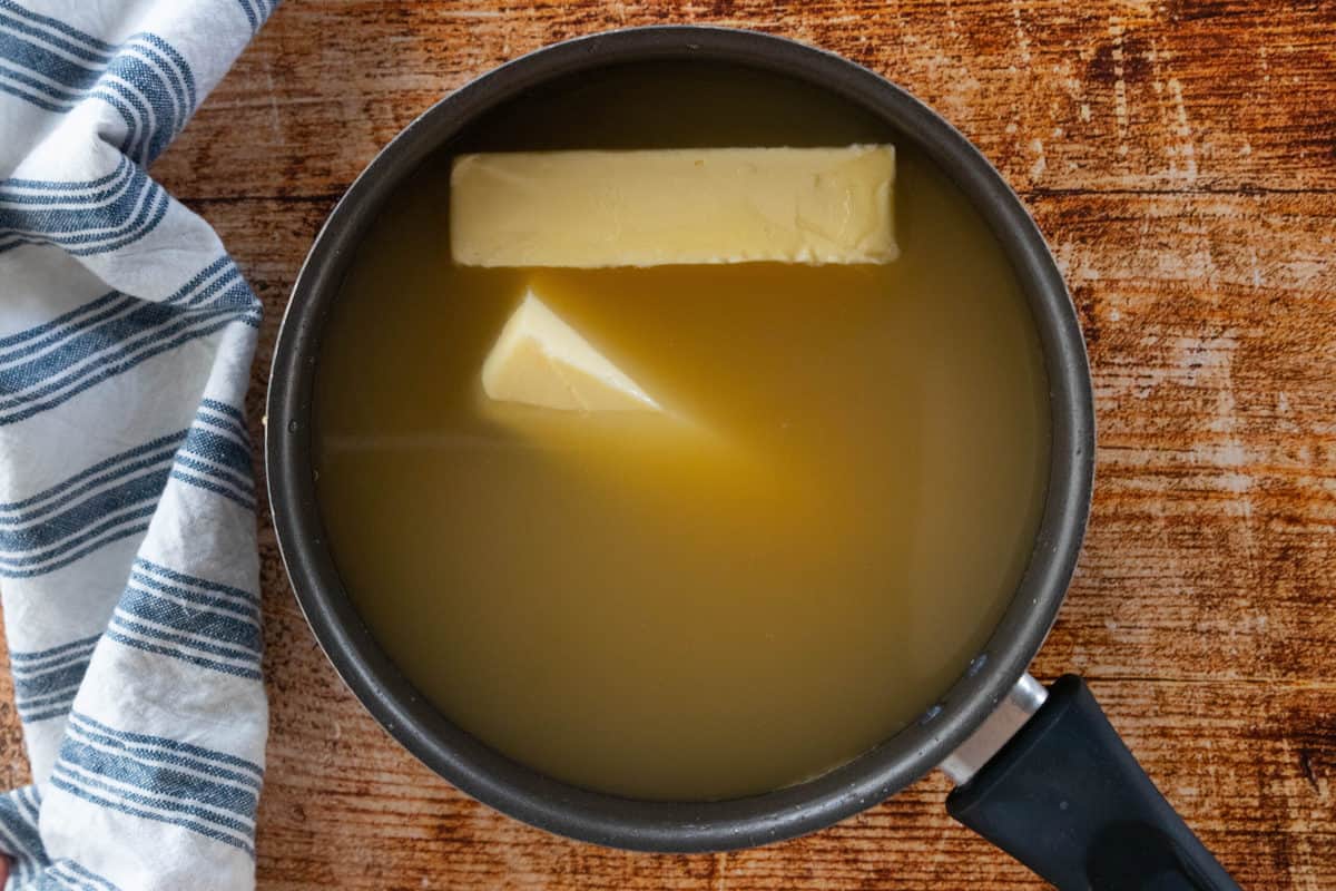 Butter being shown in a large pot filled with chicken broth. 