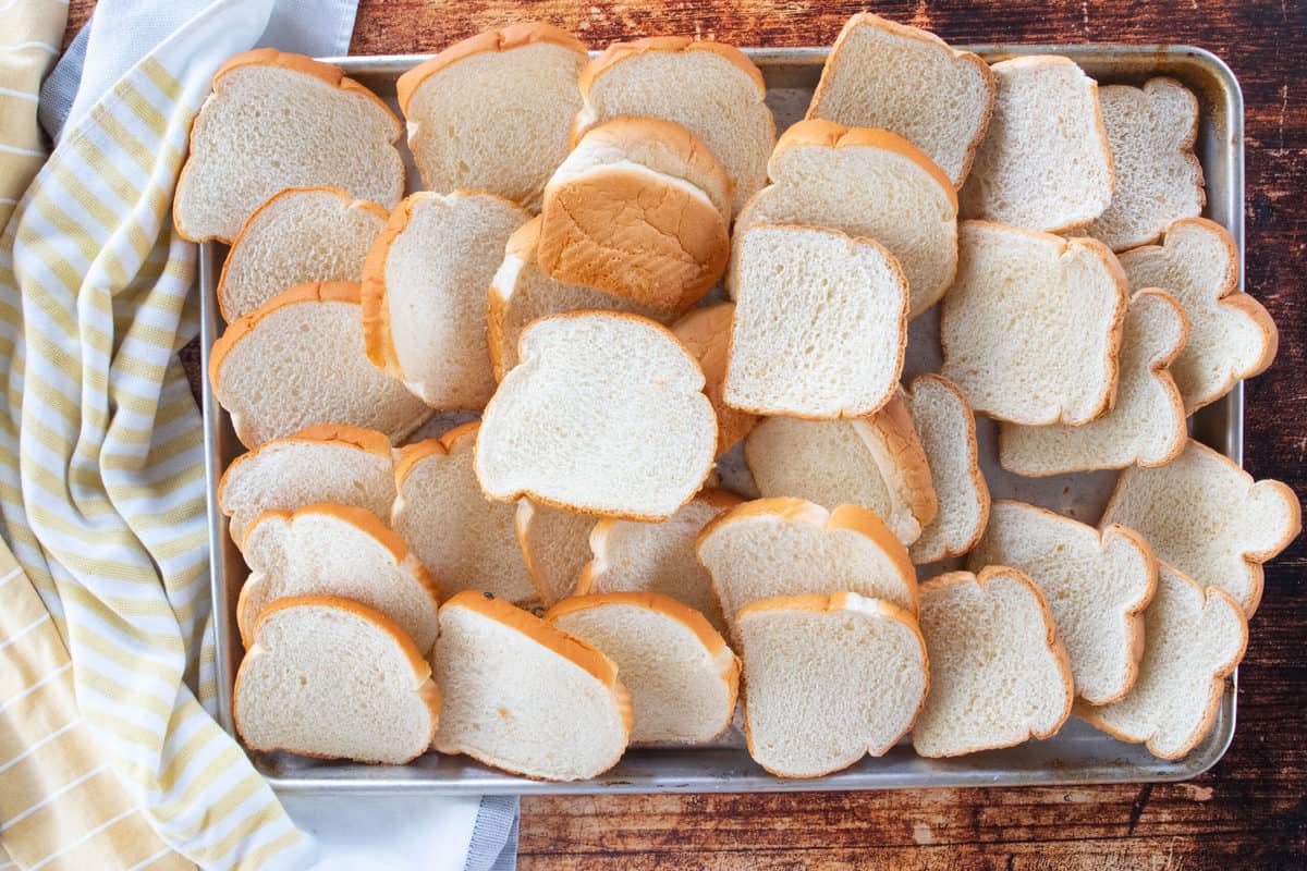 Slices of white bread spread out on a baking sheet.