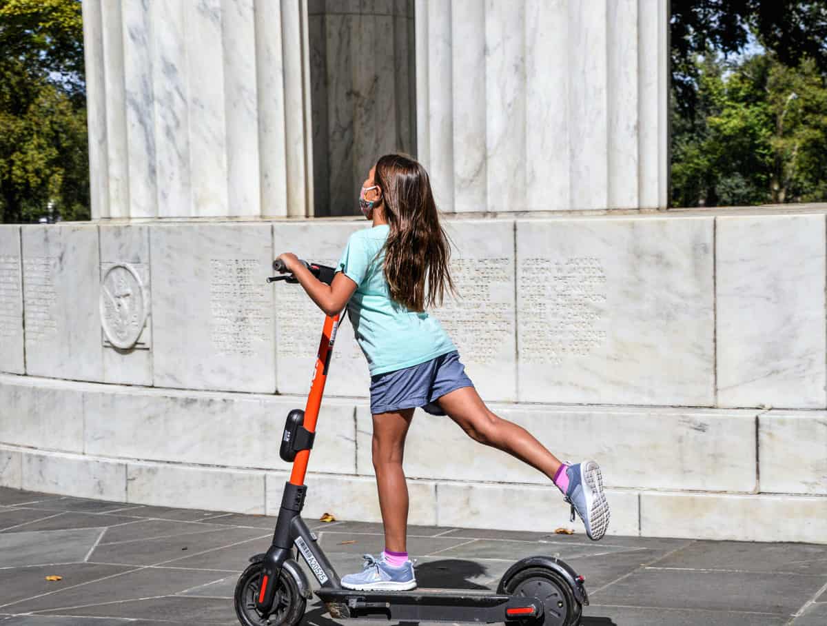Tween girl on powered scooter wearing a face mask.