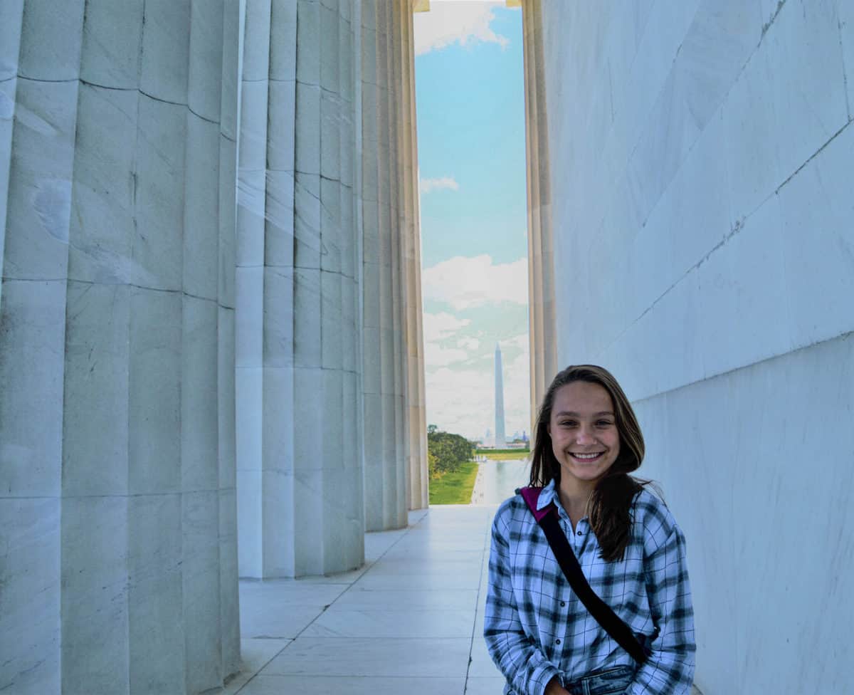 Teen girl sitting at a distance in front of the Washington Monument.
