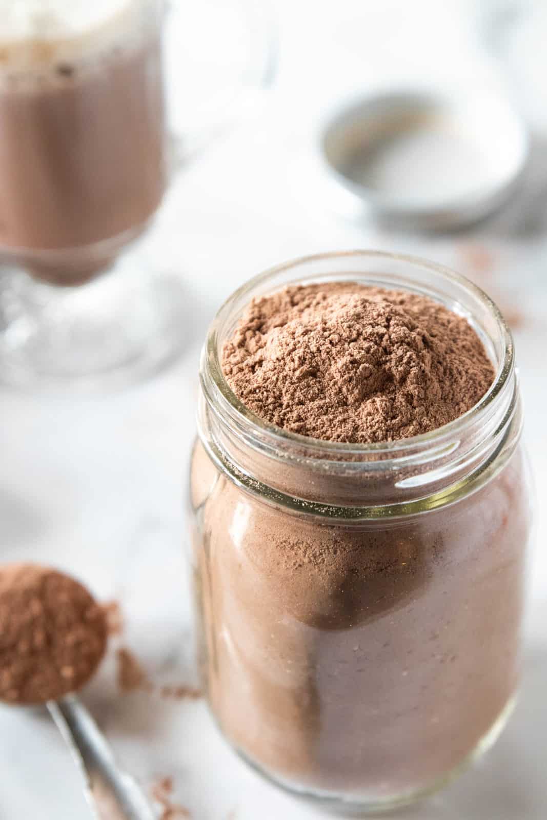 A mason jar being shown filled with homemade hot chocolate mix with a tablespoon filled with a scoop of mix next to the jar.