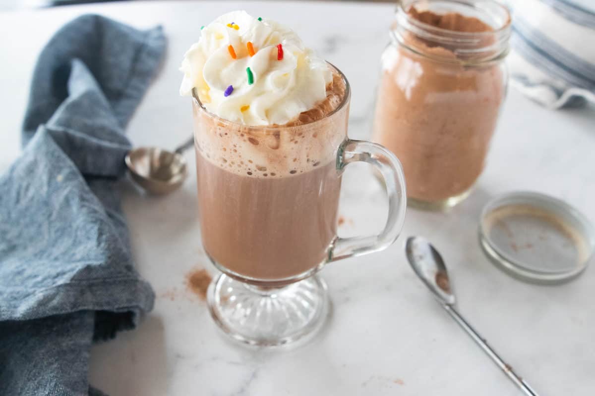 hot chocolate in a glass topped with whipped cream and sprinkles