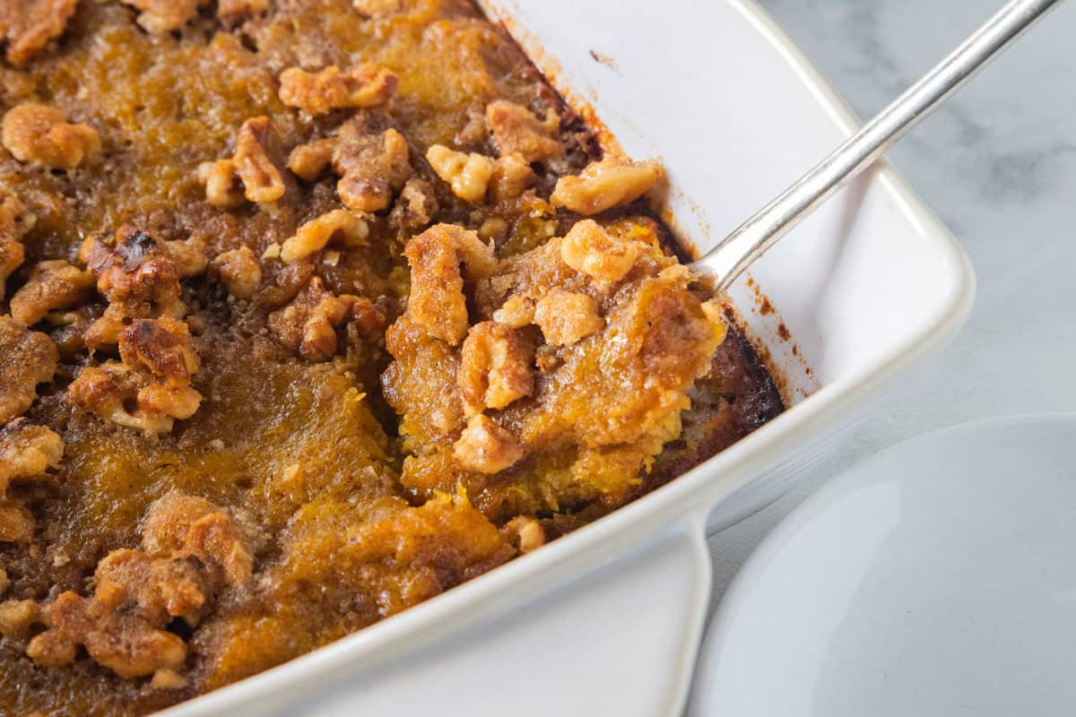 Butternut squash casserole in a white baking dish with a spoon scooping a serving from the dish.