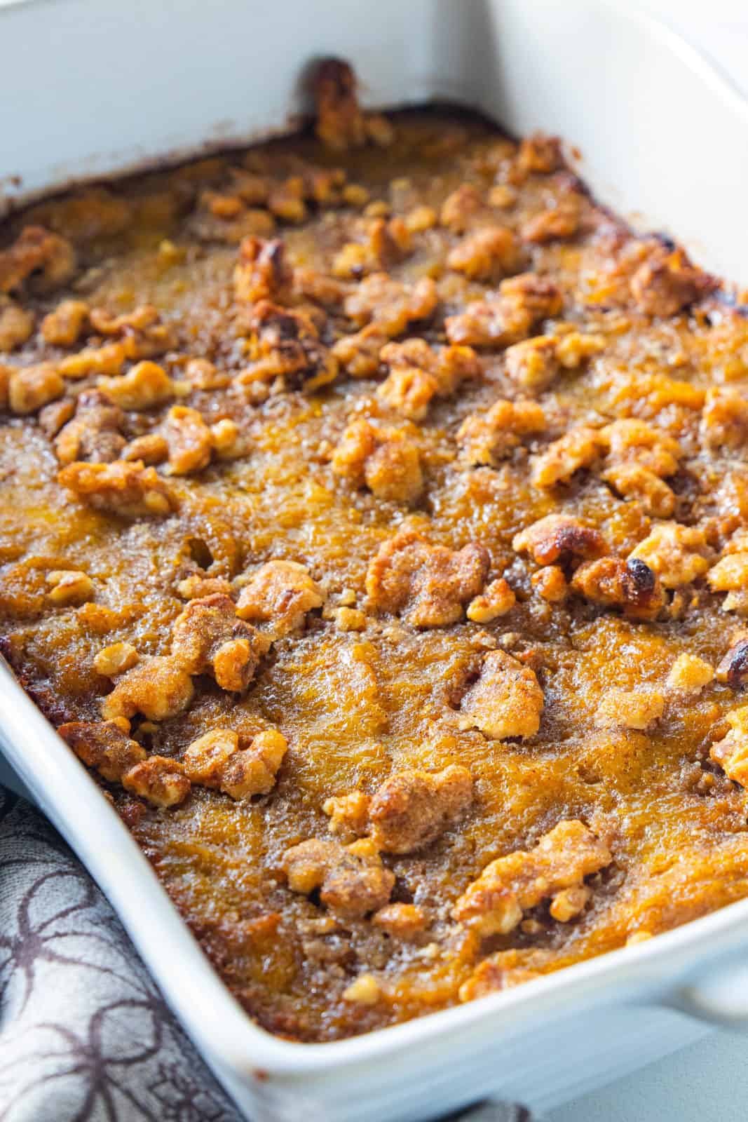 A white casserole dish filled with butternut squash casserole topped with roasted walnuts.