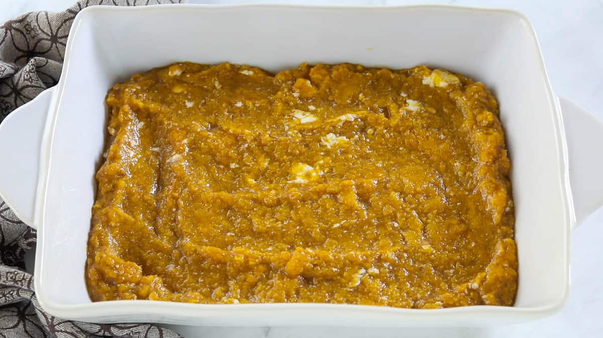 A white baking dish filled with the ingredients for butternut squash casserole.