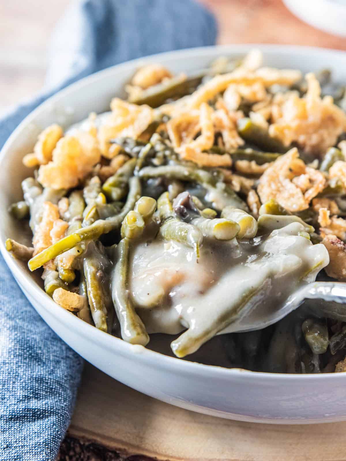 Crockpot green bean cassserole in a white serving bowl with a spoon in the bowl scooping a serving.