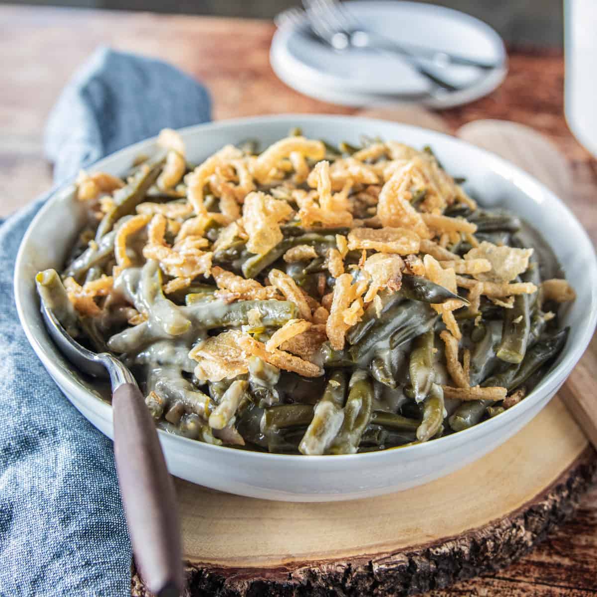 Green bean casserole topped with French fried onions in a white serving bowl with a spoon in the bowl.