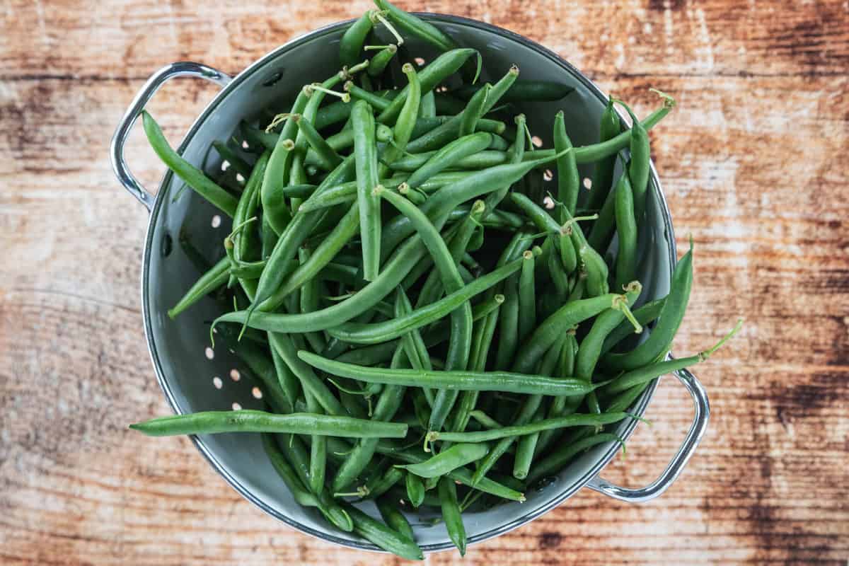 Fresh green beans in a colander that is on top of a wooden countertop.