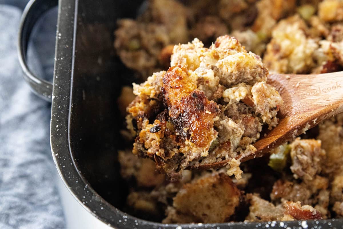 A wooden spoon scooping a serving of stuffing from a large baking pan filled with stuffing.