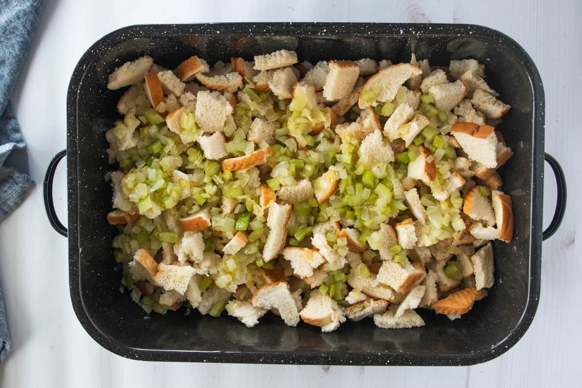 Pieces of torn white bread and diced celery in a large baking pan.