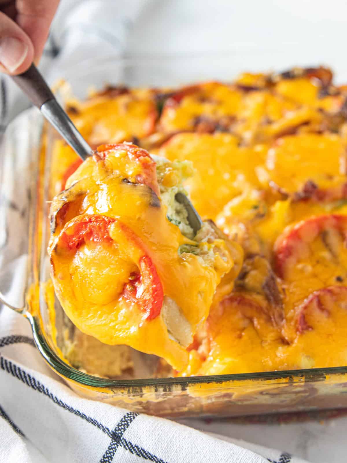 A vegetable strata recipe being shown in a glass baking dish with a serving spoon 