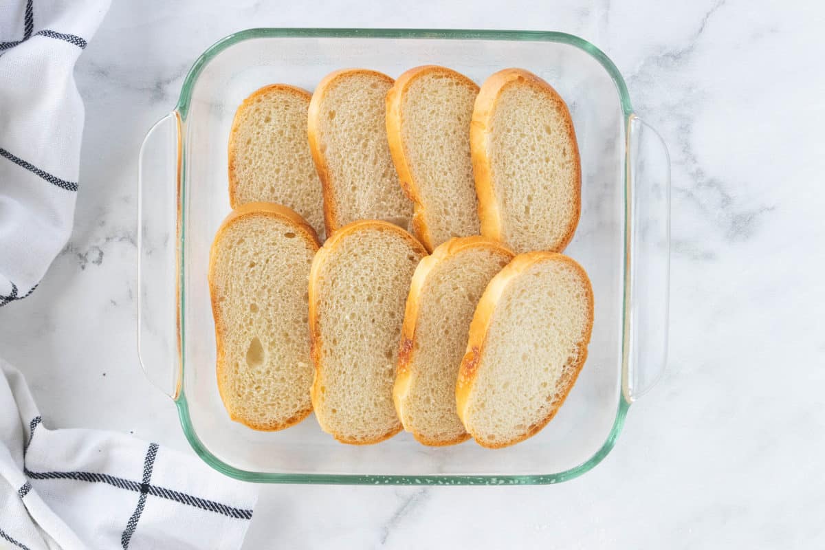 Slices of white bread in a glass baking dish that is on top of a granite countertop. 