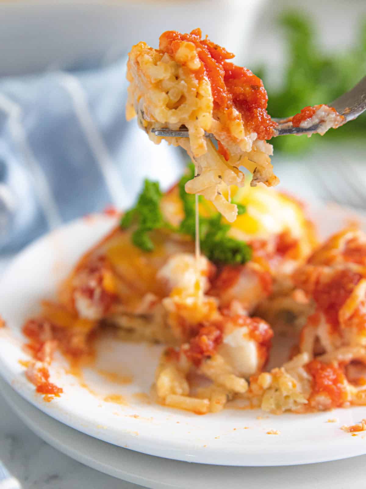 A fork scooping a bite of vegetarian baked spaghetti from a full plate.