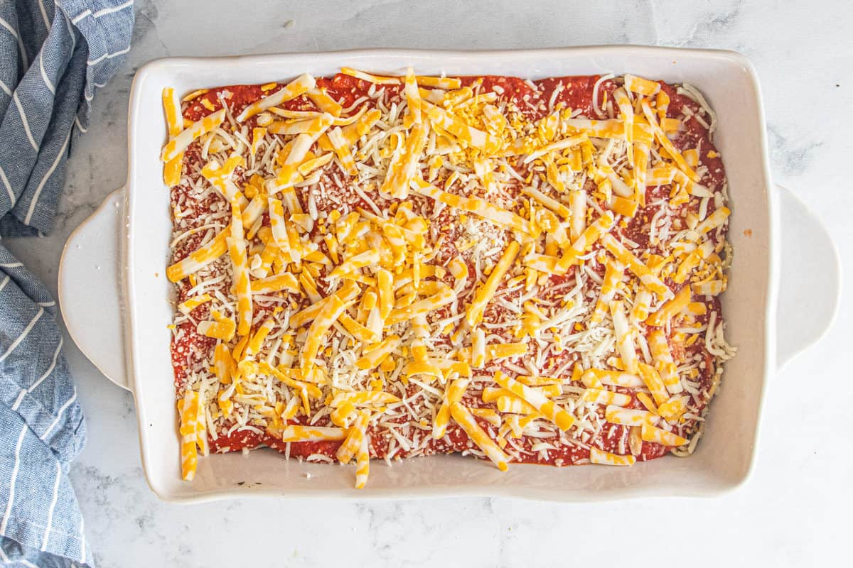 Vegetarian baked spaghetti being shown prior to being baked in a large baking dish with shredded cheese on the top.