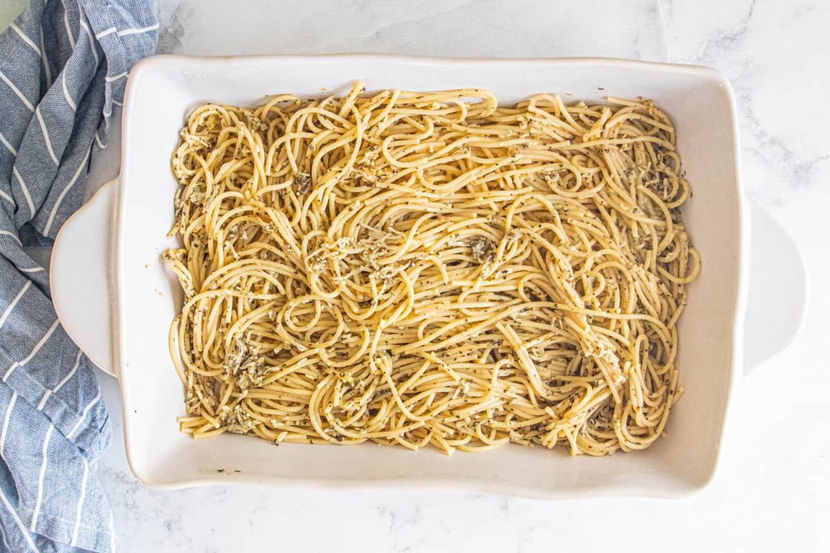 Cooked spaghetti tossed in spices being shown in a large white baking pan