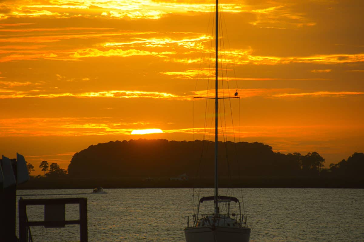 A sunset over water with a sailboat in the shadows. 