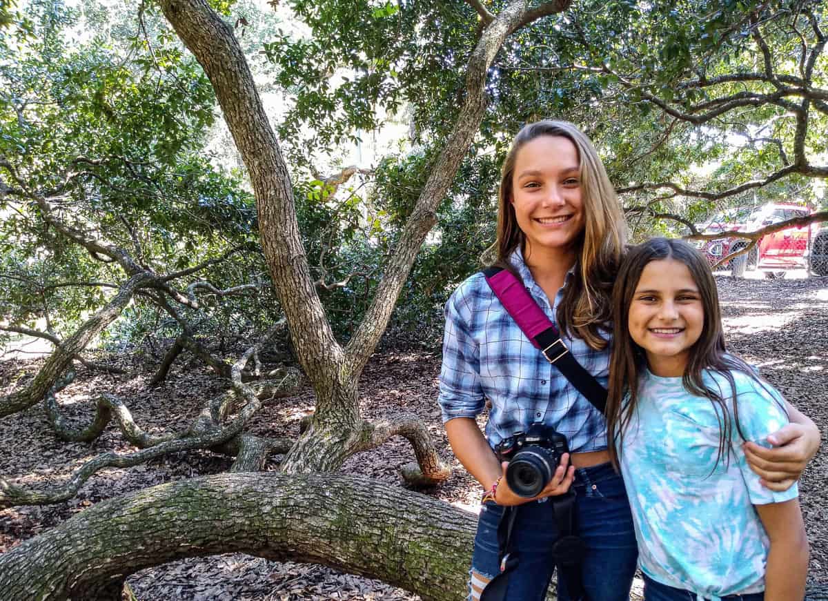 Teen girls standing in from of large trees with a camera in Charleston NC. 