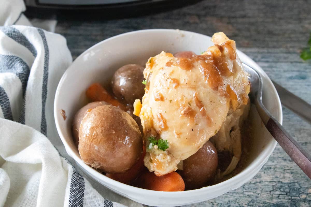 Chicken, potatoes and carrots in a white serving bowl with a fork in the bowl. 