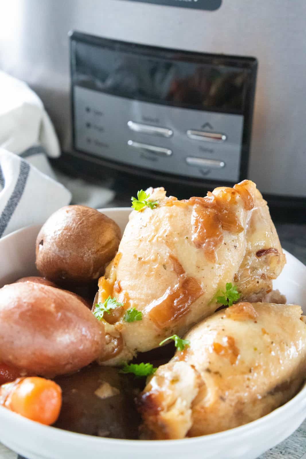 Crockpot chicken thighs and potatoes shown in a white serving bowl. 