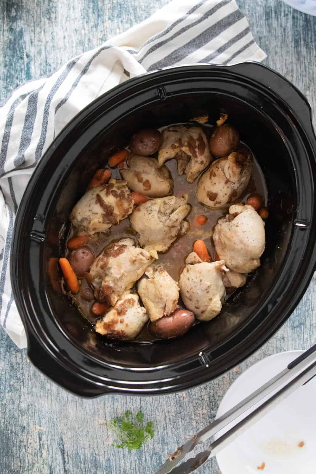 Cooked chicken thighs, red potatoes and carrots being shown in a crockpot. 