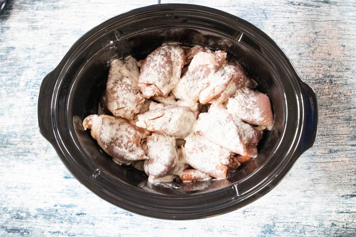 Seasoned chicken thighs being shown in a crockpot. 