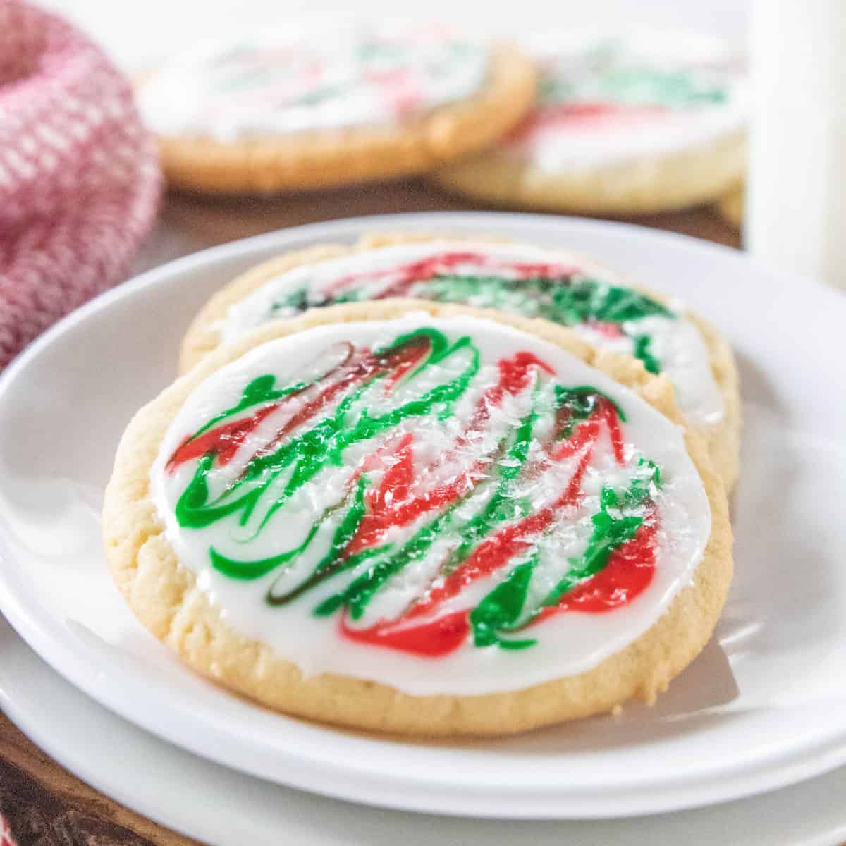 Two frosted sugar cookies being shown on a white plate. 