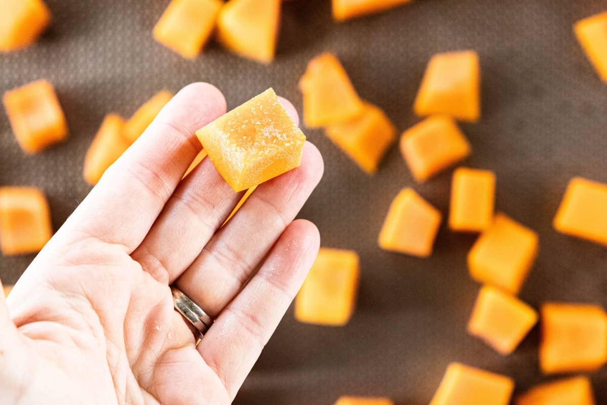 Butternut squash that has been chopped and placed on a baking sheet with a hand holding one piece. 