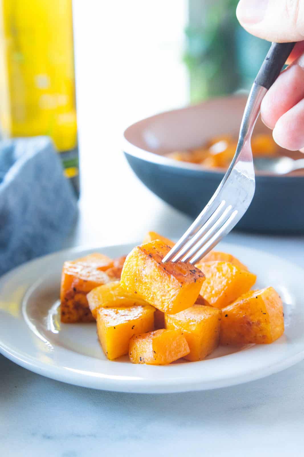 Sautéed butternut squash being shown on a white plate with a fork picking up a chunk of squash. 