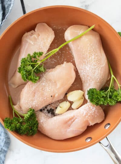 chicken breasts in a skillet with garlic, parsley stems, and salt.