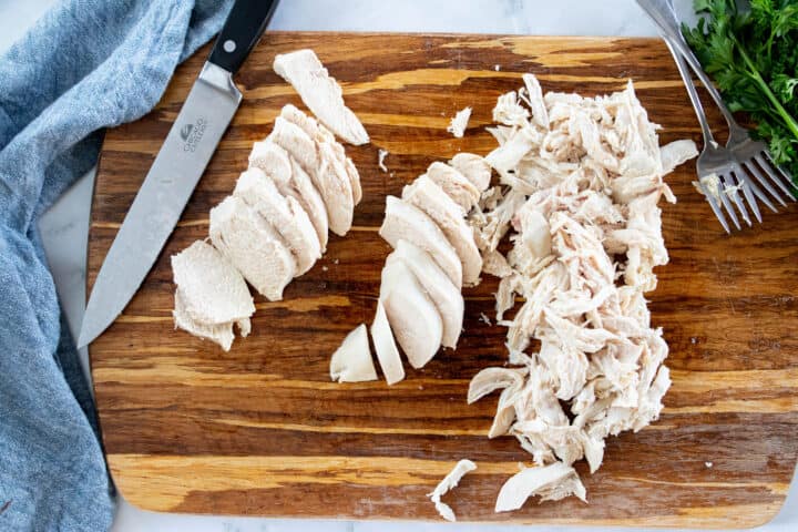 Cooked chicken breasts being shown on a cutting board, one chopped and one shredded. 