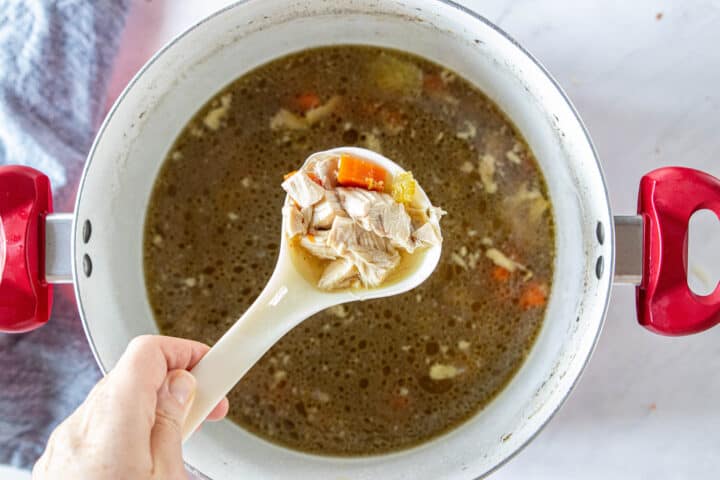 Chicken soup being shown in a large stockpot with a ladle scooping out soup. 