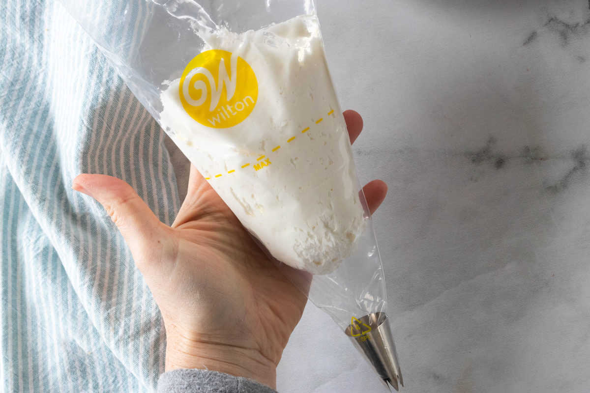 Buttercream frosting being shown in a decorating bag that is held by a hand over a granite countertop.