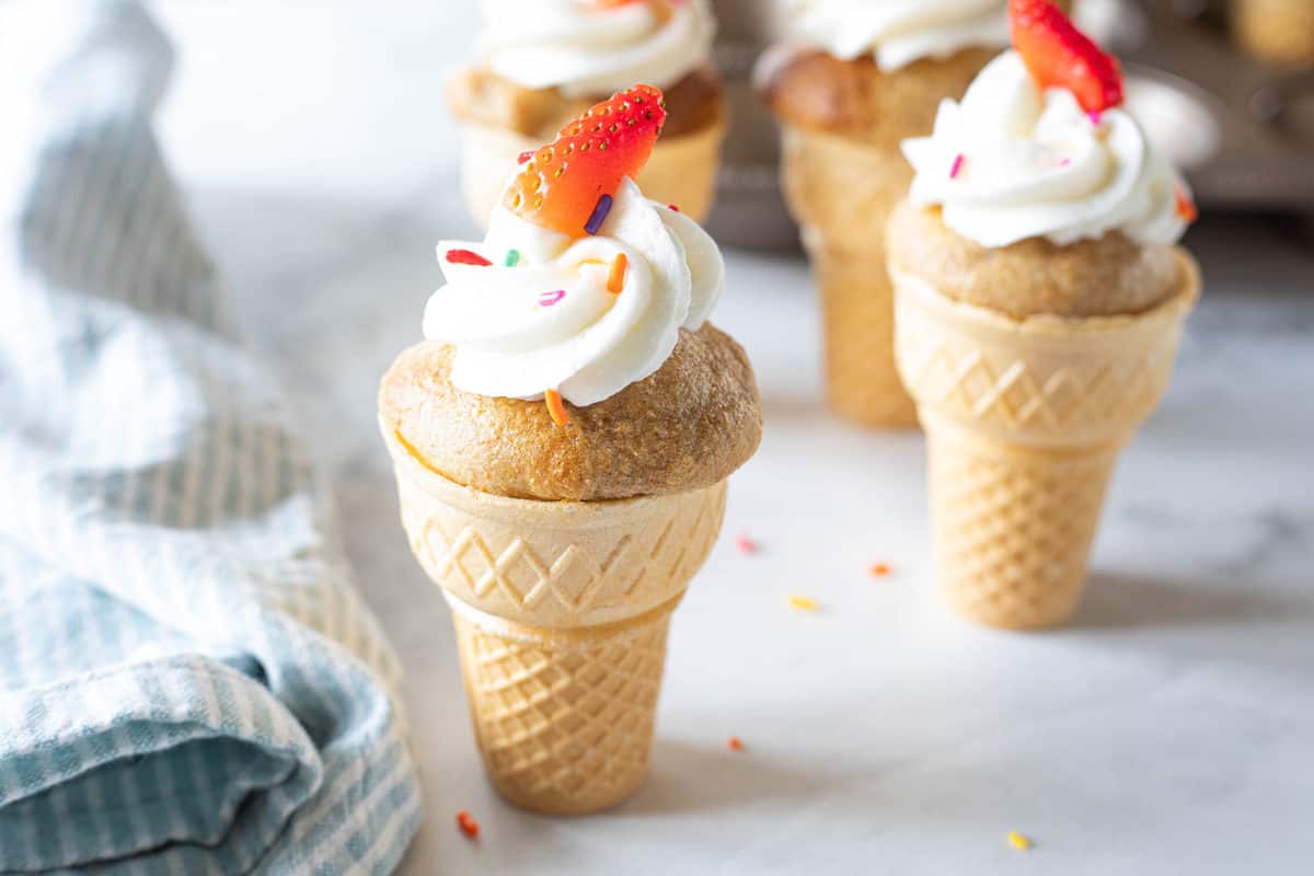 Ice cream cone cupcakes topped with almond buttercream frosting, sprinkles and a strawberry slice. 