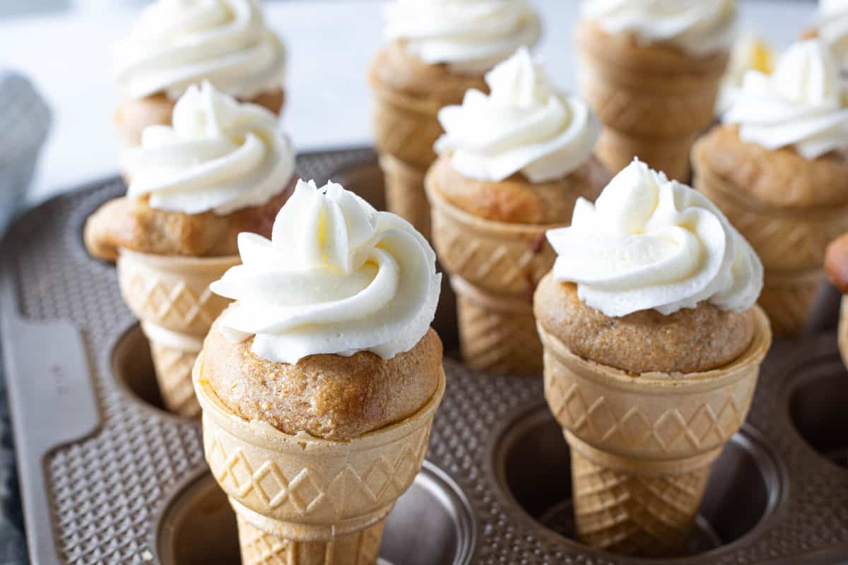 A muffin tin being shown filled with ice cream cones that are stuffed with cake and topped with buttercream frosting.